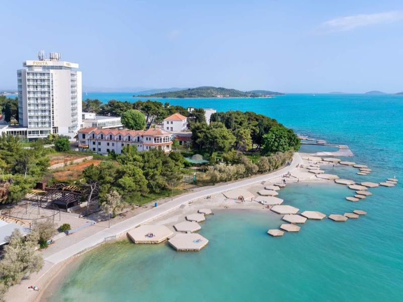 Wybrzeże z białym hotelem, plażą i czystą turkusową wodą w słoneczny dzień.