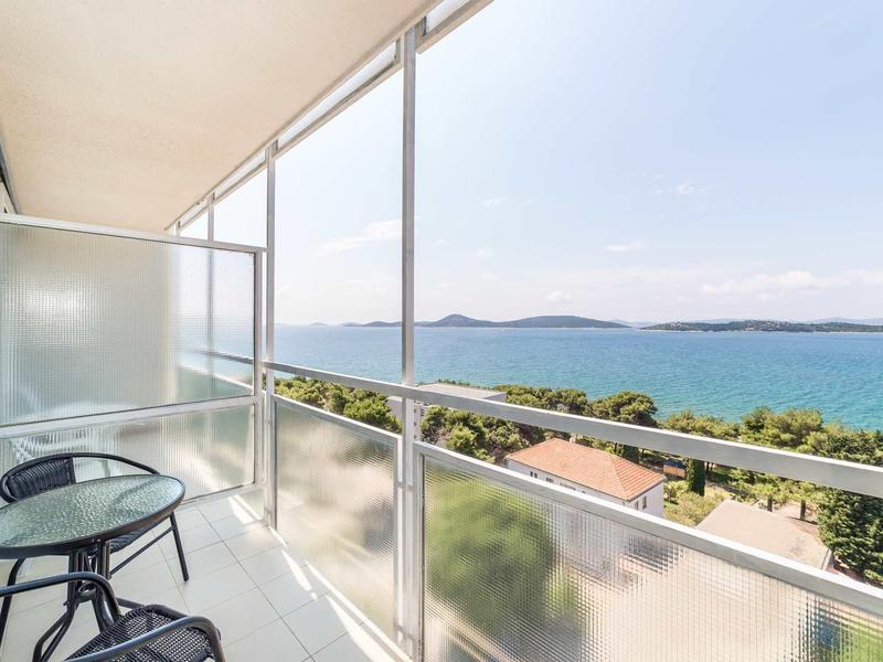 Balkon ze szklaną balustradą, dwoma krzesłami, stołem i widokiem na morze i wyspy.