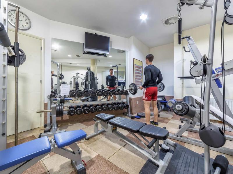 Nowoczesna siłownia z hantlami, sprzętem do ćwiczeń i mężczyzną w czerwonych spodenkach.