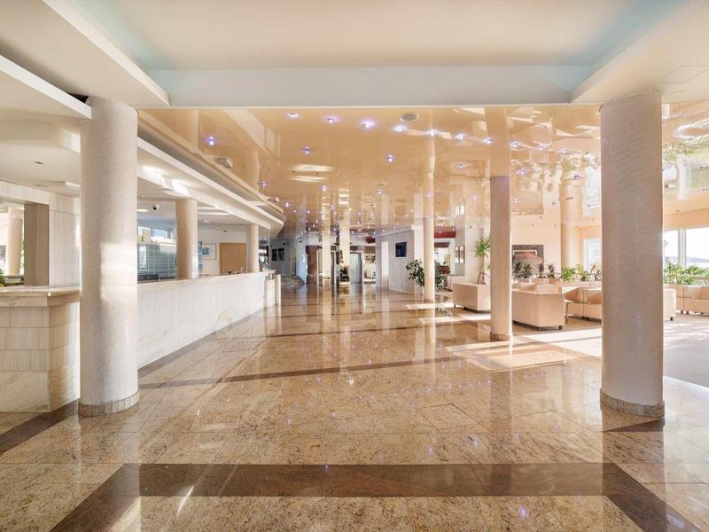 Przestronna lobby hotelowa z marmurową podłogą, białymi kolumnami i jasną atmosferą.