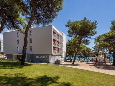 Modernes Hotelgebäude mit roten Balkonen neben einem bewaldeten Strandbereich an der Küste.