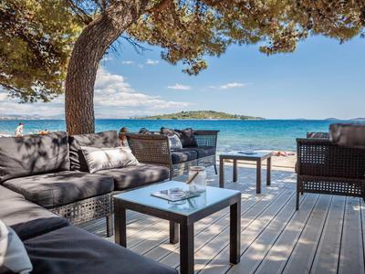 Gemütliche Sitzgruppe mit Sofas und Tischen auf Holzterrasse mit Meerblick und Baum