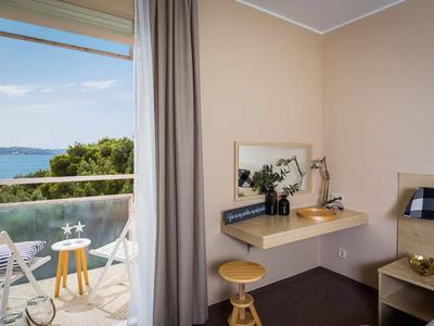 Helles Zimmer mit Schreibtisch, Spiegel, Hocker und Balkon mit Meerblick und Stühlen.