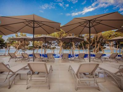 Sonnenschirme und Liegestühle am Pool mit Bäumen im Hintergrund bei blauem Himmel.