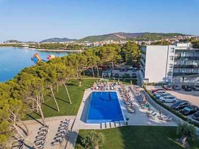 Hotel con grande piscina rettangolare, lettini, alberi e vista mare.