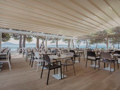 Überdachter Außenbereich eines Restaurants mit Blick aufs Meer und leeren Tischen.