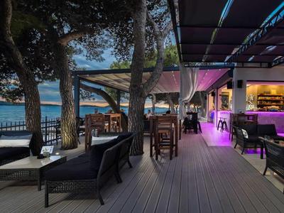 Freiluftrestaurant mit Holzboden, gemütlichen Stühlen und Tischen, beleuchtet mit buntem Licht.