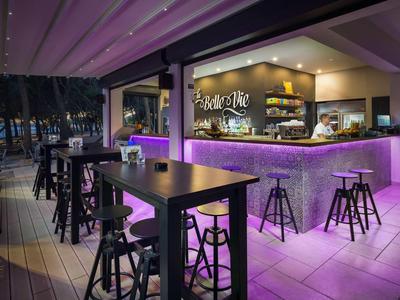 Moderner Außenbarbereich mit lila Beleuchtung, schwarzen Möbeln und Bartresen bei Nacht.