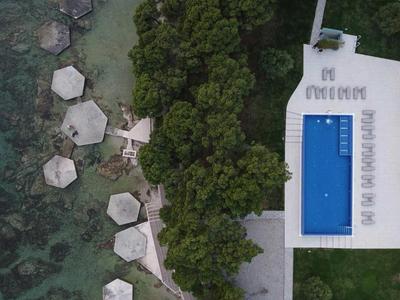 Luftaufnahme eines Resorts mit blauem Pool, umgeben von Bäumen und mehreren Holzstegen über Wasser.