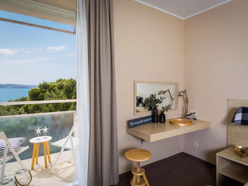 Helles Zimmer mit Schreibtisch, Spiegel, Hocker und Balkon mit Meerblick und Stühlen.