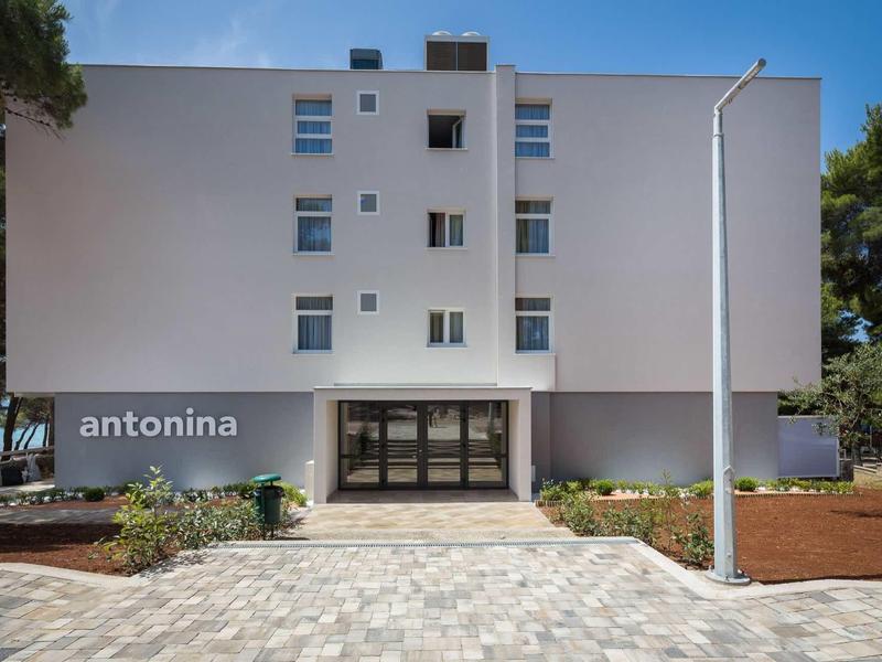 Modernes vierstöckiges Wohngebäude mit weißen Wänden und vielen Fenstern vor blauem Himmel.