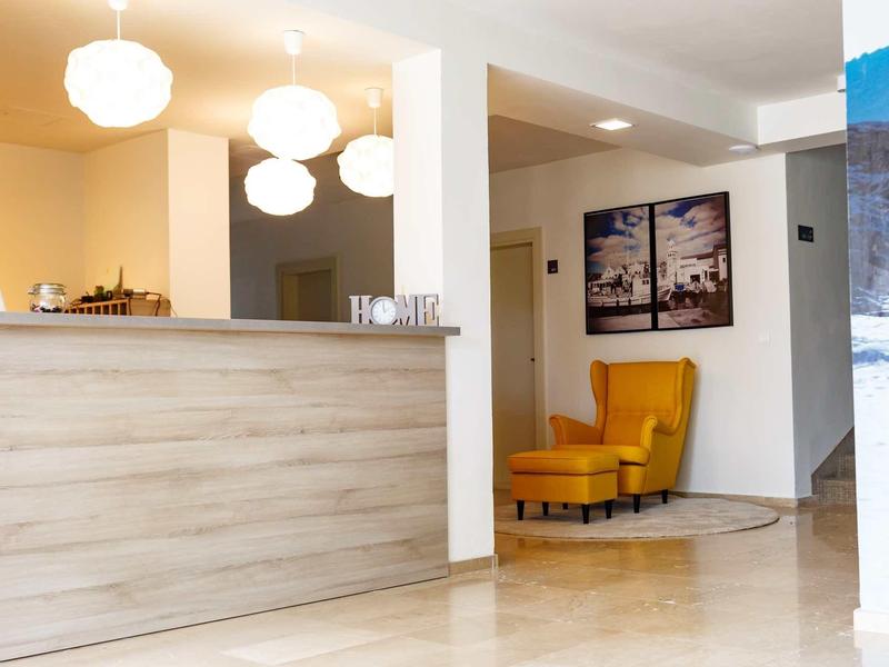 Helle Rezeption mit Holztheke, drei rundlichen Deckenlampen und gelbem Sessel vor Wandbildern.