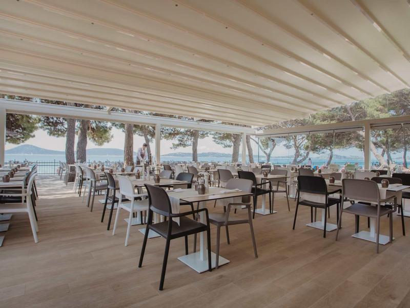 Offenes Restaurant mit Holzboden, schwarzen und weißen Stühlen unter einem weißen Dach.