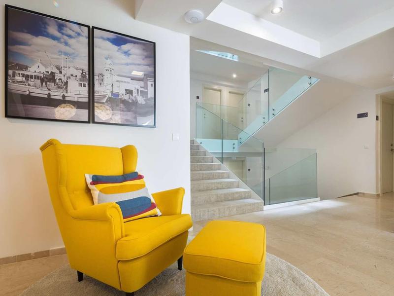 Moderner Raum mit gelbem Sessel, passendem Hocker, künstlerischen Bildern und heller Treppe aus Glas.