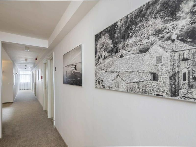 Heller Flur mit weißen Wänden, Teppichboden und zwei schwarz-weißen Landschaftsbildern an der Wand.