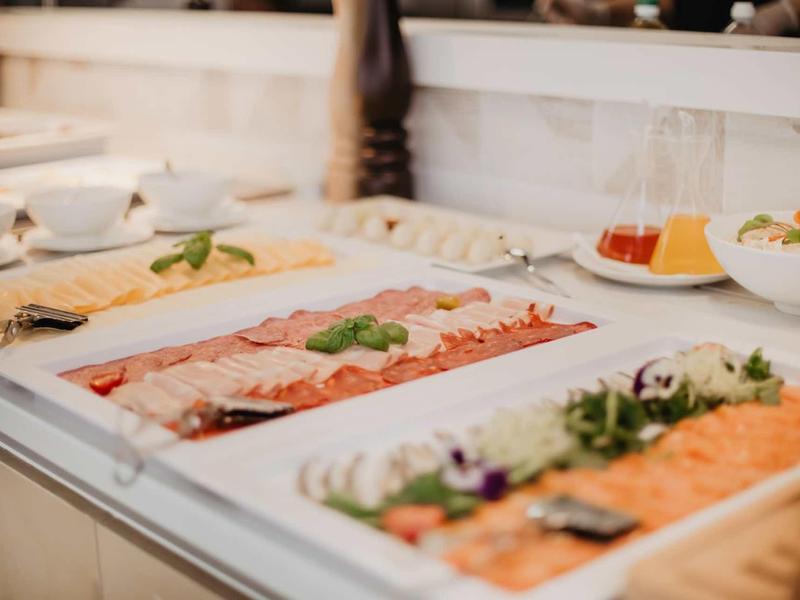 Buffet mit aufgeschnittenem Lachs, Wurst, Kräutern und Sauce auf weißen Tellern angerichtet.