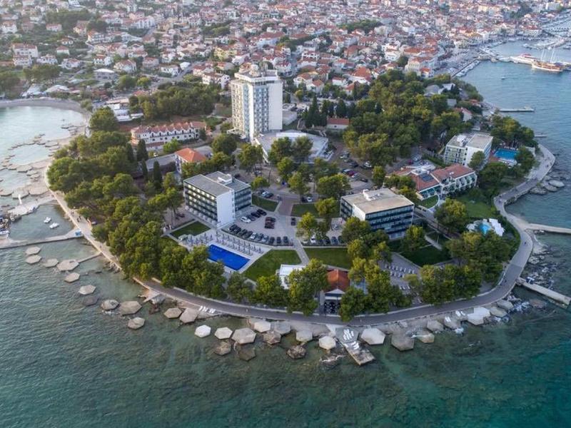 Kleine Insel mit dichtem Baumbestand, Gebäuden und Stränden, umgeben von klarem Meerwasser.