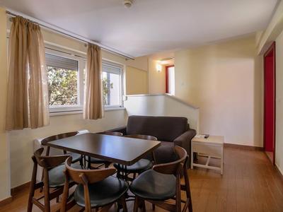 Een lichte eetruimte met een donkerbruine tafel, vijf stoelen en een beige bank voor twee ramen.