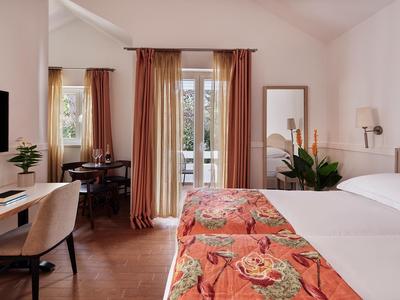 Helles Hotelzimmer mit Queensize-Bett, floralem Betthaupt und Balkon mit Blick nach draußen.