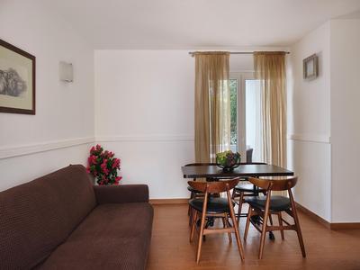 Helles Esszimmer mit brauner Couch, Holztisch und Stühlen vor bodentiefem Fenster mit Gardinen.