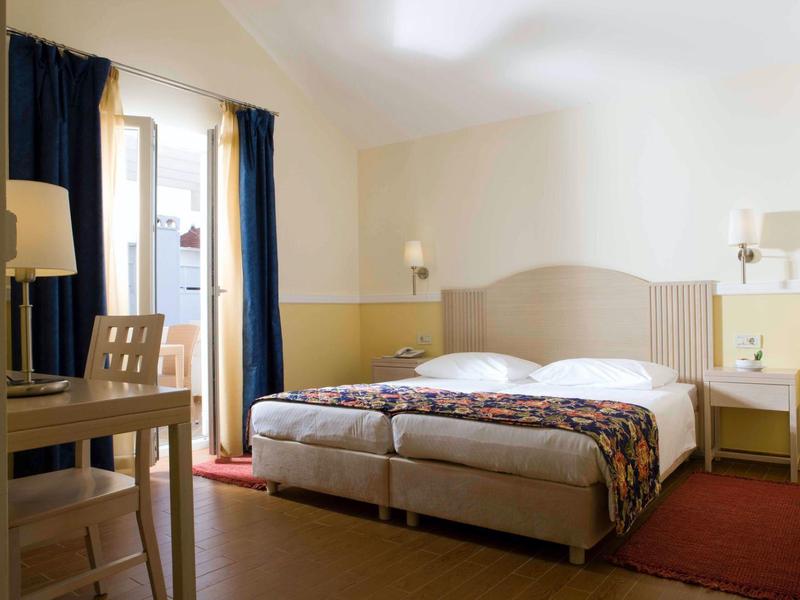 Lichte hotelkamer met twee eenpersoonsbedden, een bureau en een raam met gordijnen.