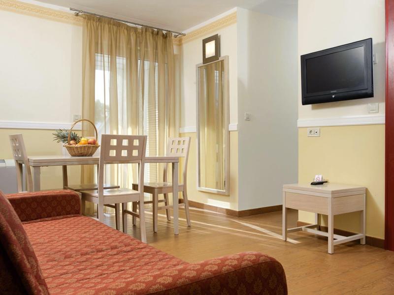 Gezellig woongedeelte met bank, eettafel en tv in een hotelkamer.