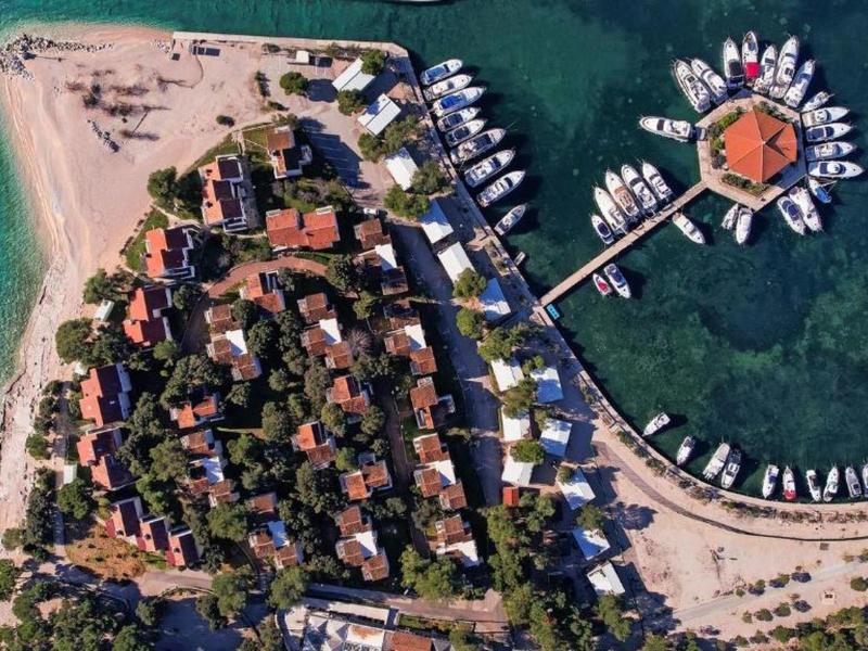 Luchtfoto van een eiland met bungalows, een pier en helder turquoise water.