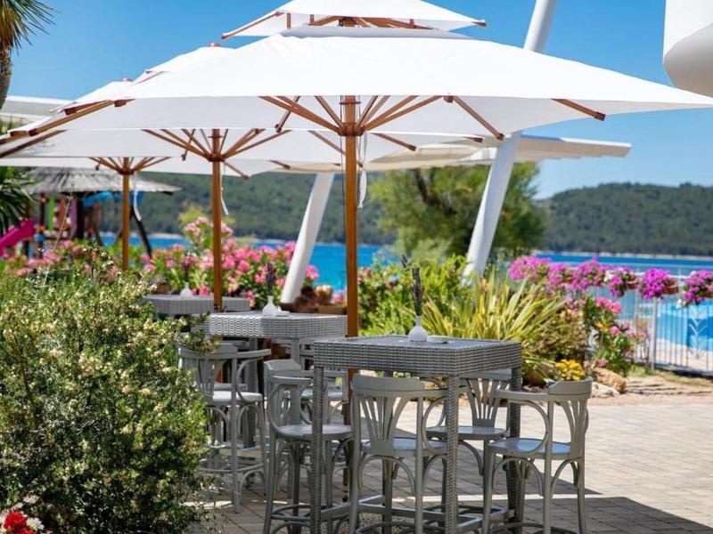 Terrascafé met witte parasols met uitzicht op blauw water en groene heuvels.