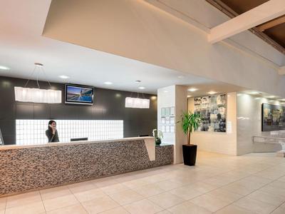 Modern hotel lobby with reception desk, illuminated walls, and a potted plant.