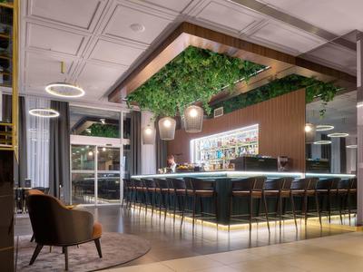 Moderne hotelbar met houten accenten, groene plafonddecoratie en stijlvolle zitjes.