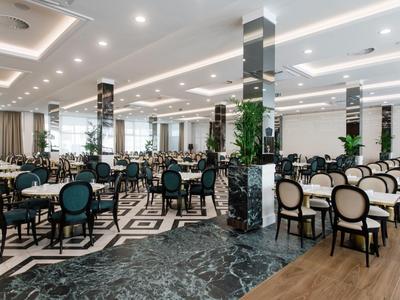 Grote, moderne eetzaal met elegante tafels, stoelen en marmeren zuilen.