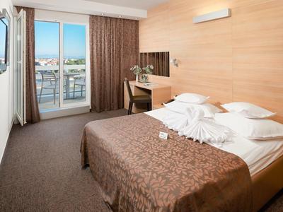 Moderne hotelkamer met tweepersoonsbed, bureau, balkon en uitzicht op de stad.