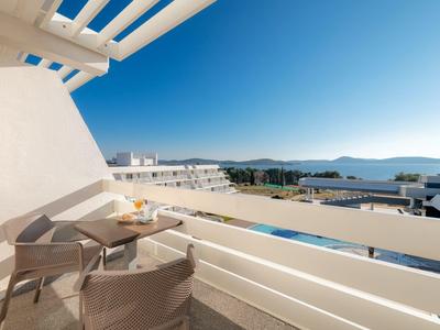 Balkon met stoelen en tafel, uitzicht op zee en witte gebouwen onder heldere lucht.