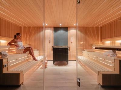 Moderne sauna met houten wanden, banken en een vrouw die ontspant.
