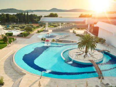 Hotelzwembad met ronde eiland en palmbomen bij zonsondergang met uitzicht op zee.