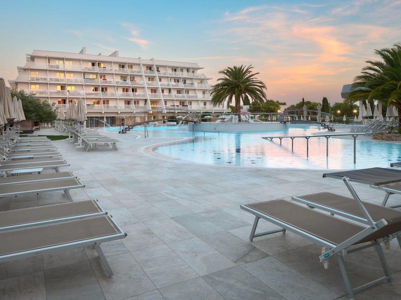 Modern hotelzwembad met ligstoelen en palmbomen bij zonsondergang.