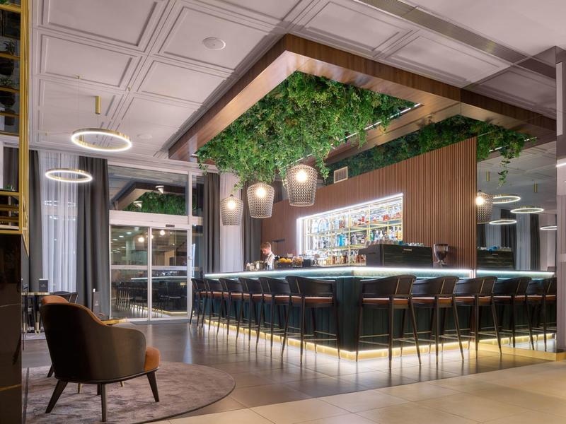 Moderne hotelbar met houten accenten, groene plafonddecoratie en stijlvolle zitjes.