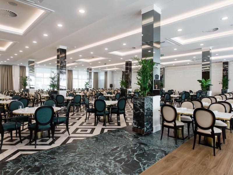 Grote, moderne eetzaal met elegante tafels, stoelen en marmeren zuilen.