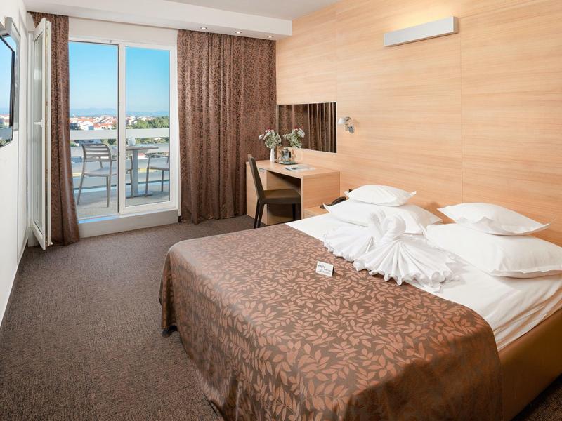 Moderne hotelkamer met tweepersoonsbed, bureau, balkon en uitzicht op de stad.