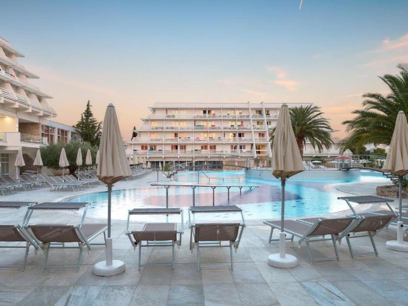 Hotelzwembad met ligstoelen en parasols voor een meerlaagse hotelgebouw bij zonsondergang.