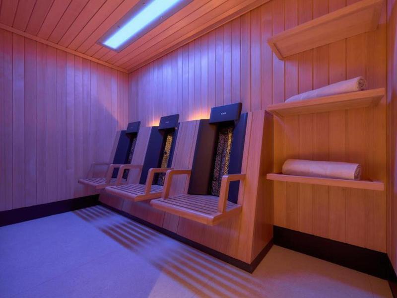 Saunaruimte met houten wanden, drie ligstoelen, planken en zacht blauw licht.