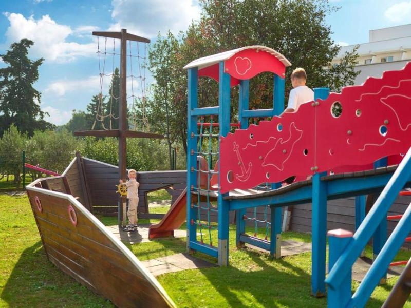 Buitenspeeltuin met scheepsvorm, glijbaan en klimrek bij zonnig weer.