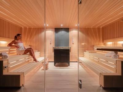 Moderne Sauna mit hellem Holz, zwei Etagen Bänken und entspannter Frau links.