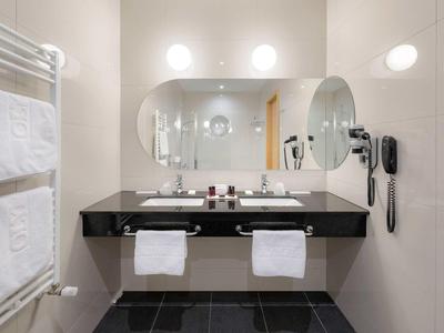 Moderner Badezimmerspiegel mit zwei Waschbecken, Handtüchern und Haartrockner an heller Wand.