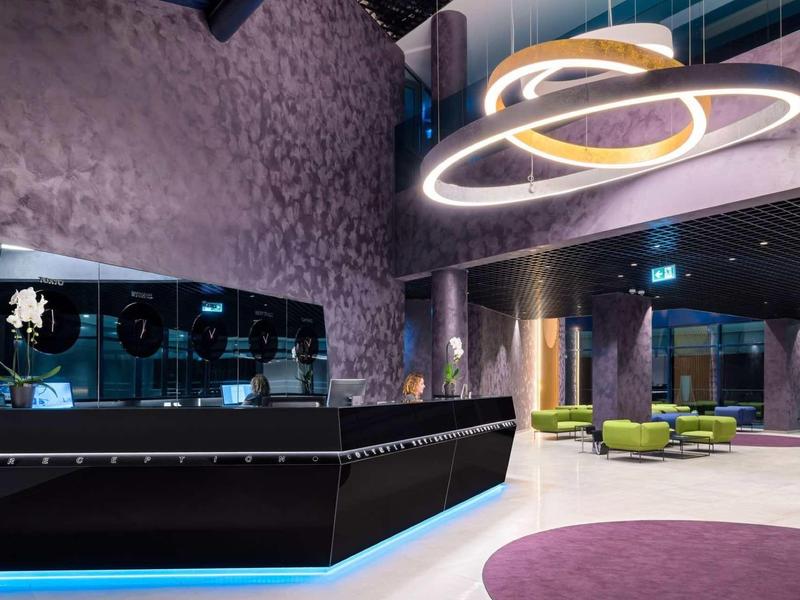 Moderner Empfangsbereich mit violettem Wandakzent, schwarzem Tresen und grüner Sitzgruppe.