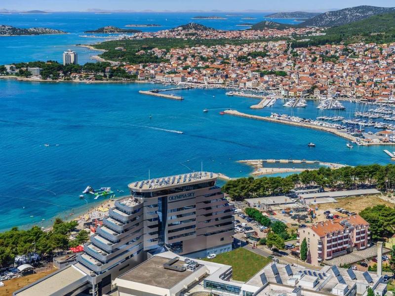 Blick auf eine Küstenstadt mit blauem Meer, Hafen, vielen Booten und dicht bebauten Gebäuden.