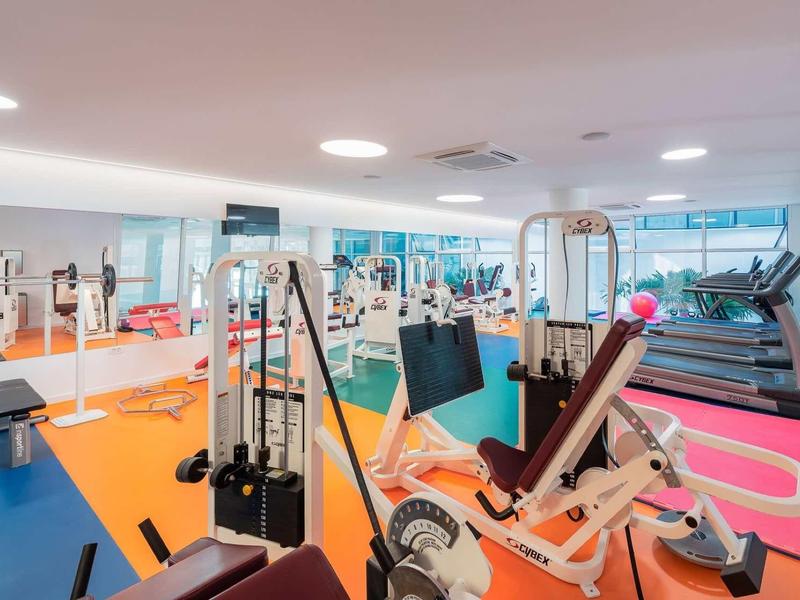 Modernes Fitnessstudio mit diversen Geräten, Hanteln und Laufbändern, helle Räume und bunte Böden.