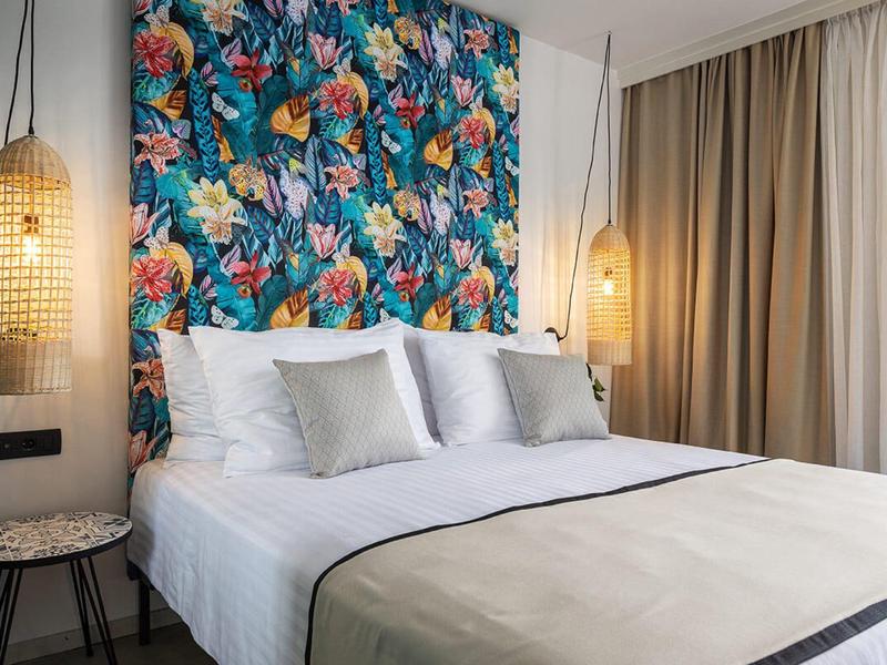 Modernes Schlafzimmer mit großem Bett, buntem Blumen-Motiv an der Wand und warmen Hängelampen.