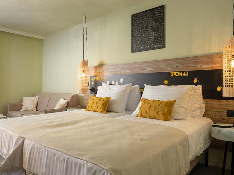 Gemütliches Schlafzimmer mit zwei Einzelbetten, gelben Kissen, Holzpaneel und warmen Hängelampen.