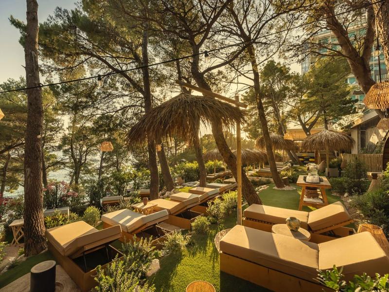 Gemütliche Liegestühle und Sonnenschirme zwischen hohen Bäumen mit Blick auf das Wasser.